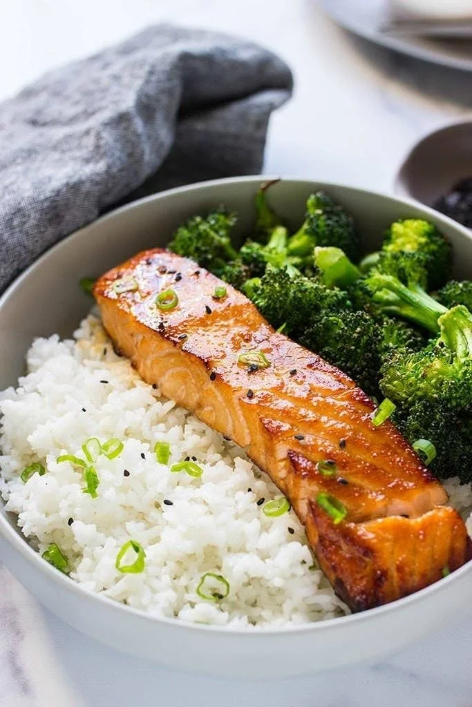 Honey garlic salmon dish served with rice and steamed broccoli on a plate.