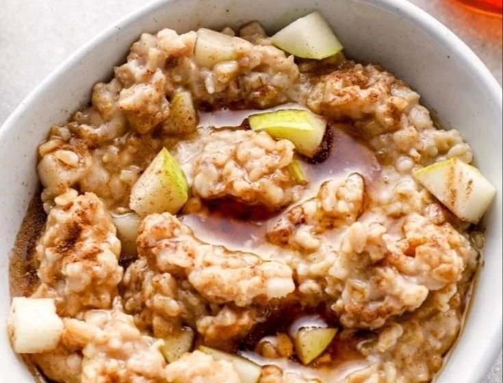 Bowl of spiced pear oatmeal topped with cinnamon and walnuts.